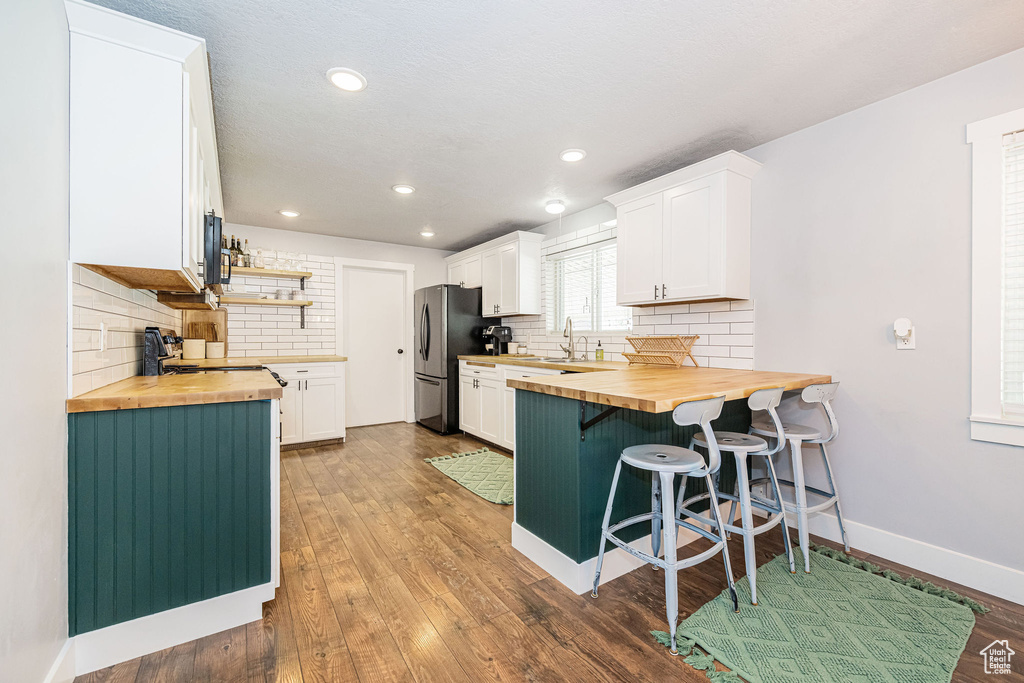 Kitchen featuring wooden counters, freestanding refrigerator, a breakfast bar area, tasteful backsplash, and open shelves
