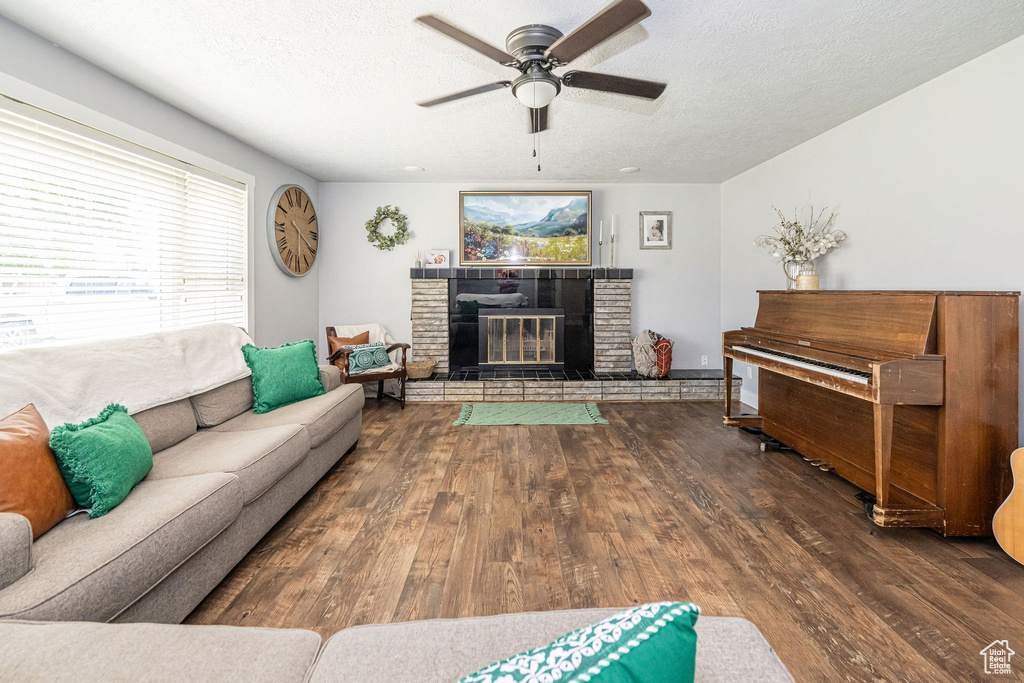 Living room with wood finished floors, ceiling fan, a glass covered fireplace, a textured ceiling, and healthy amount of natural light
