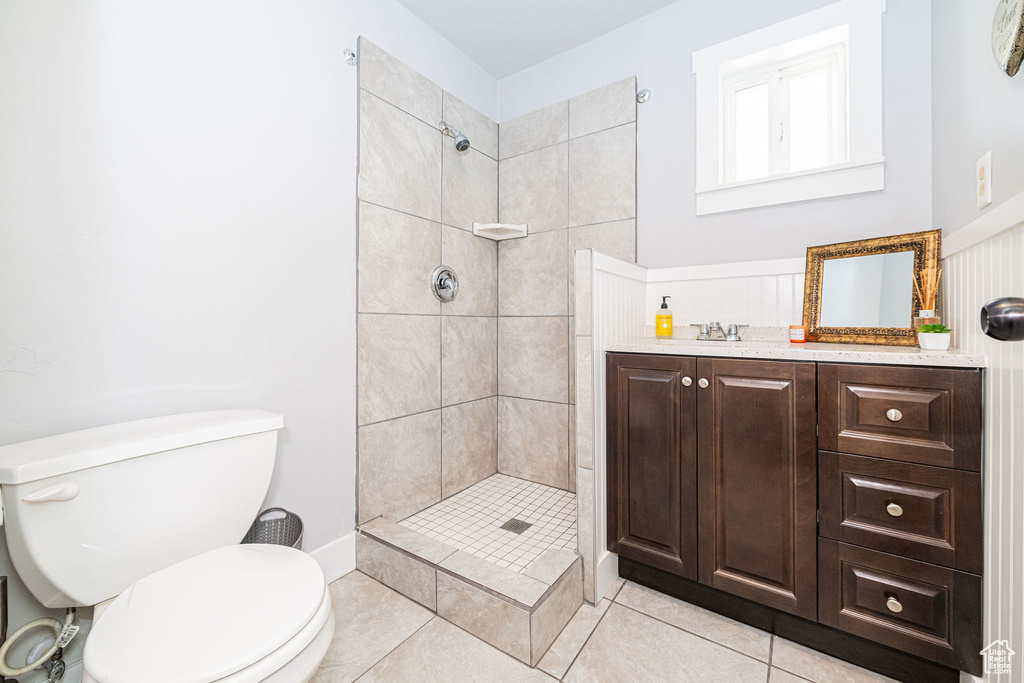 Bathroom featuring toilet, tiled shower, tile patterned floors, and vanity