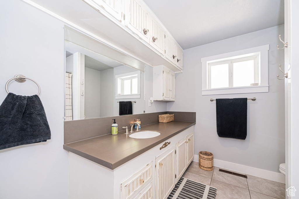 Full bathroom with healthy amount of natural light, tile patterned flooring, baseboards, and vanity