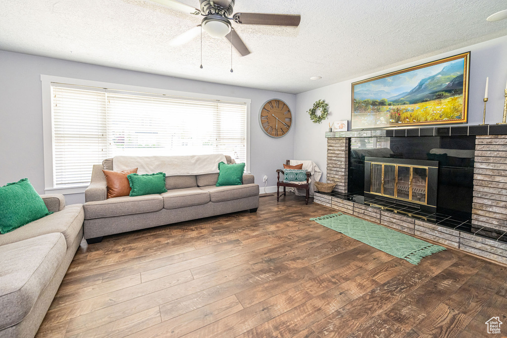 Living area with a textured ceiling, ceiling fan, wood finished floors, and a fireplace