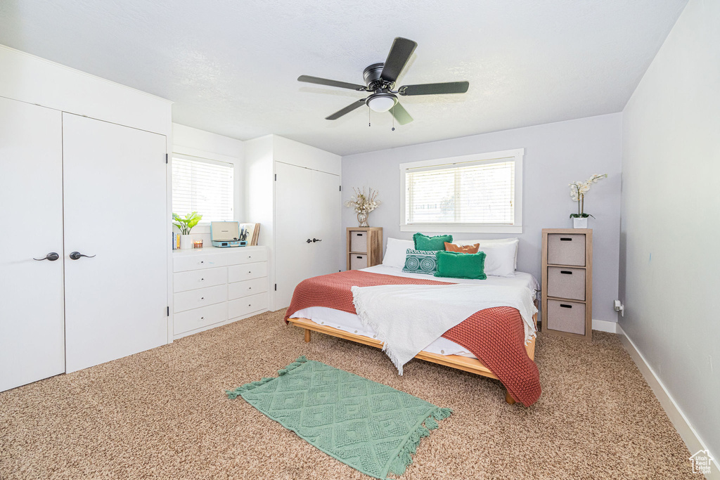 Bedroom with multiple closets, multiple windows, carpet floors, and ceiling fan