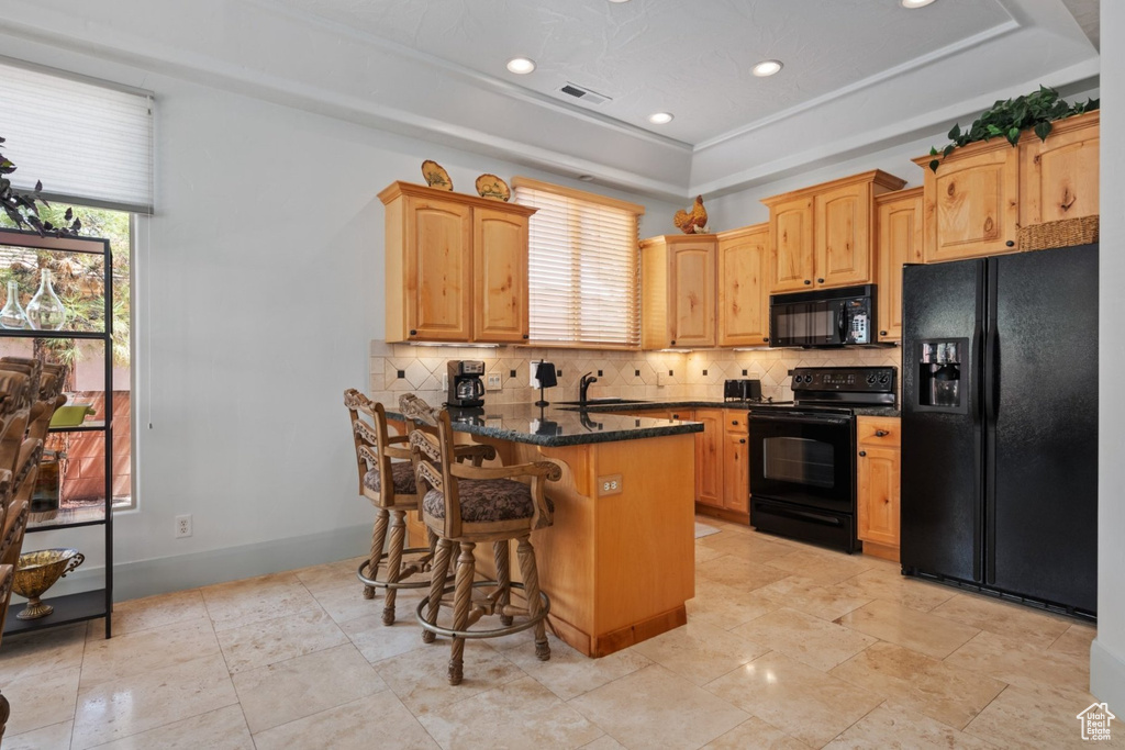 Kitchen featuring black appliances, a sink, backsplash, a breakfast bar area, and a tray ceiling
