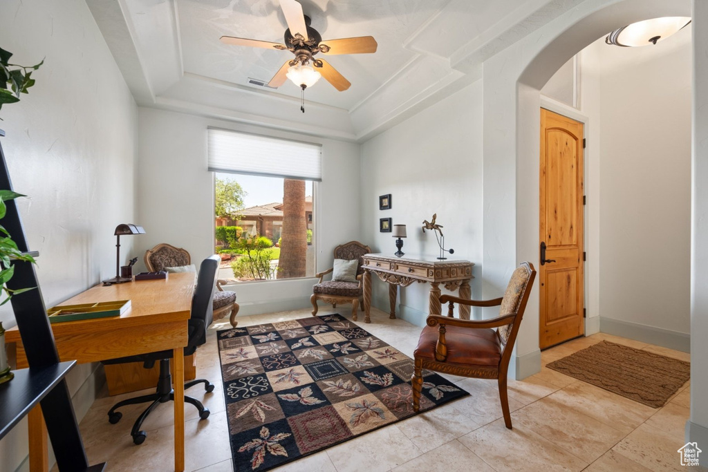 Home office featuring arched walkways, ceiling fan, and a tray ceiling
