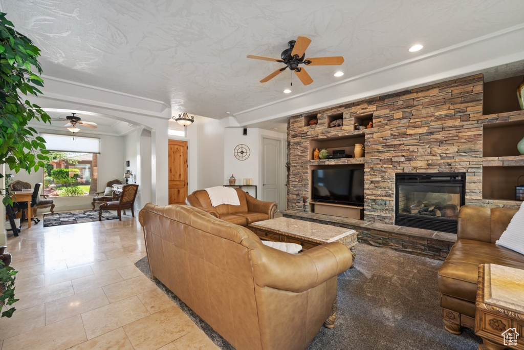 Living room with ceiling fan, arched walkways, a stone fireplace, recessed lighting, and tile patterned flooring