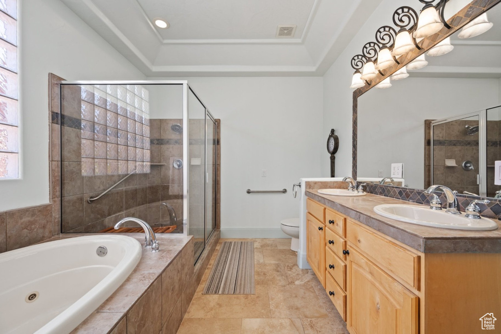 Bathroom featuring a stall shower, a jetted tub, double vanity, toilet, and a raised ceiling