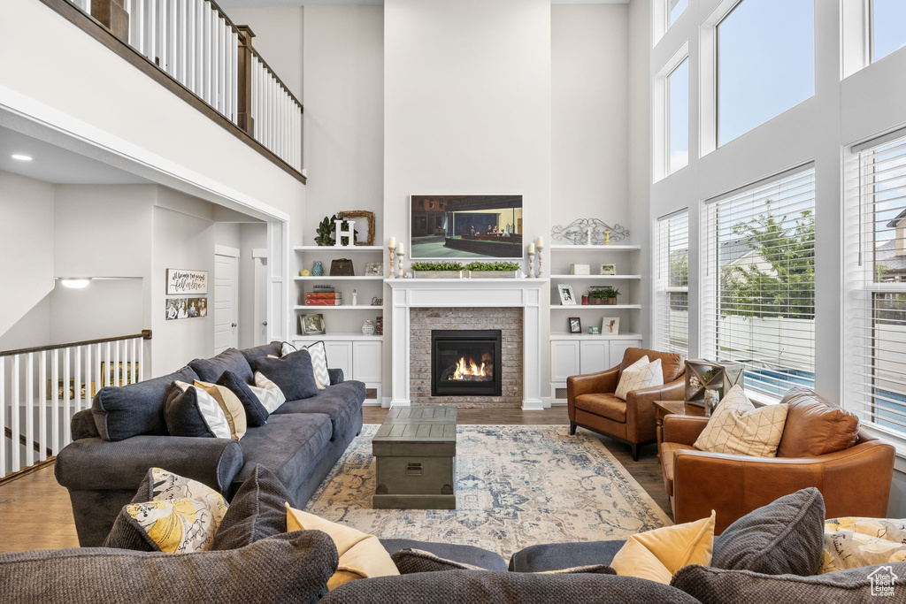 Living room with a high ceiling, wood finished floors, a glass covered fireplace, and built in features