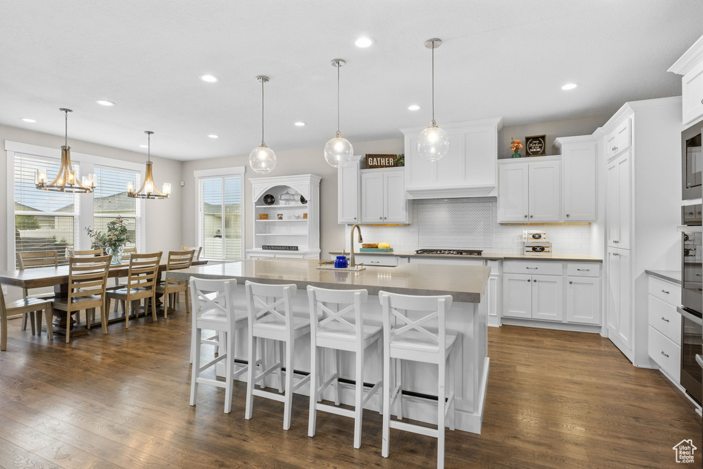 Kitchen featuring a sink, backsplash, gas cooktop, a breakfast bar area, and a kitchen island with sink