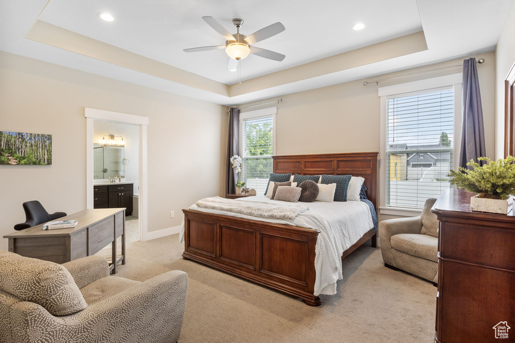 Bedroom with a tray ceiling, light colored carpet, ensuite bathroom, recessed lighting, and a ceiling fan