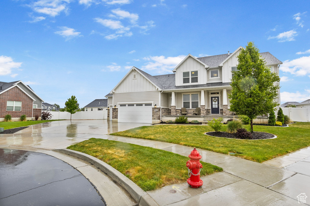 Craftsman-style house with board and batten siding, driveway, covered porch, stone siding, and a garage
