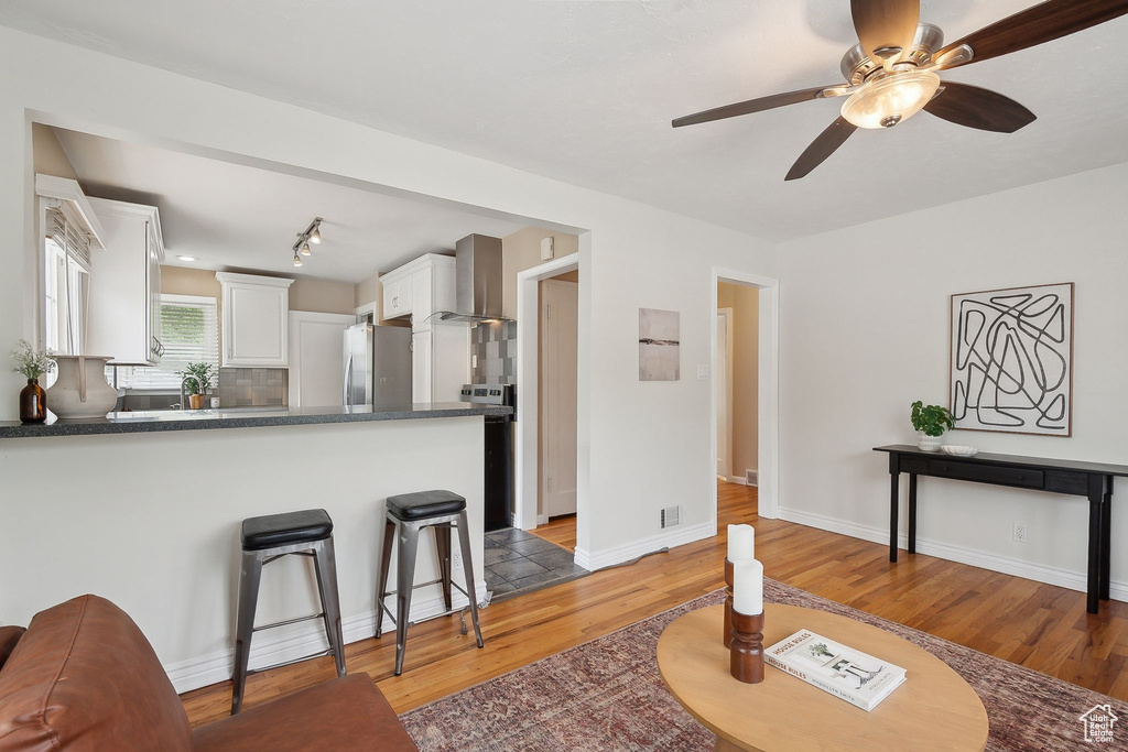 Kitchen featuring freestanding refrigerator, wall chimney exhaust hood, light wood finished floors, white cabinets, and dark countertops