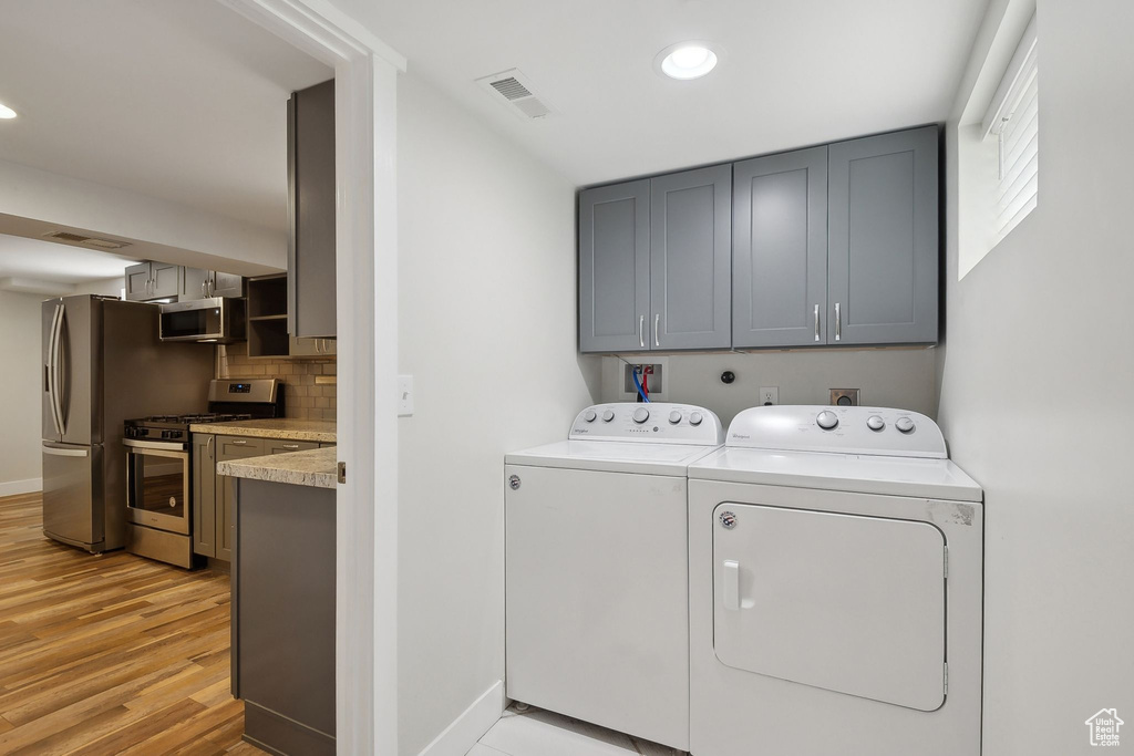 Clothes washing area featuring washing machine and dryer, light wood-type flooring, baseboards, cabinet space, and recessed lighting