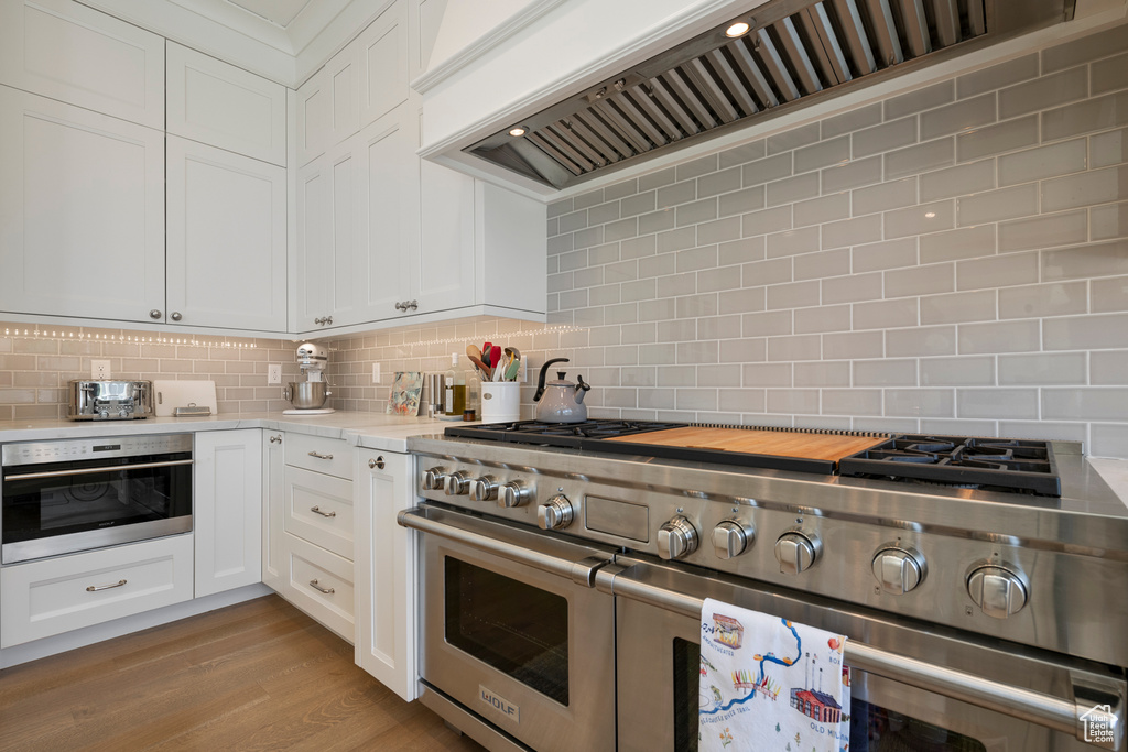 Kitchen with stainless steel appliances, custom exhaust hood, decorative backsplash, and white cabinetry