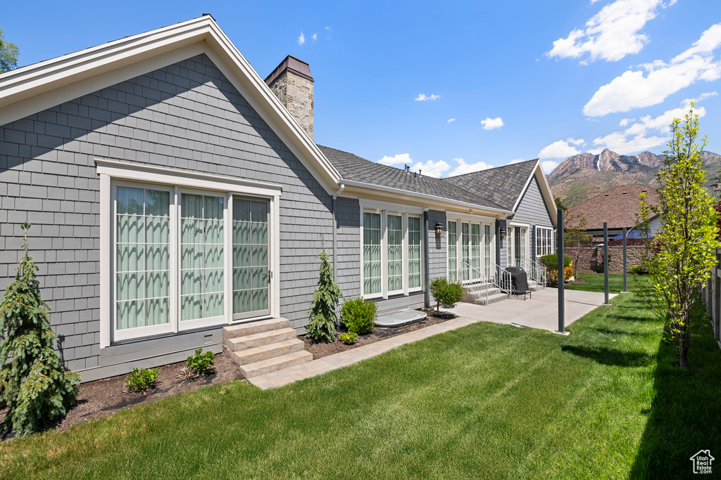 Rear view of house with entry steps, a patio, a chimney, a mountain view, and a shingled roof