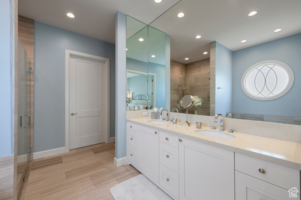 Ensuite bathroom featuring tiled shower, recessed lighting, double vanity, wood finished floors, and baseboards