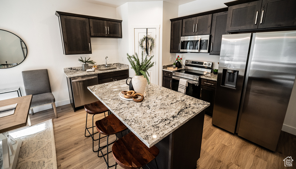 Kitchen featuring stainless steel appliances, a kitchen bar, light stone countertops, and light wood-style floors