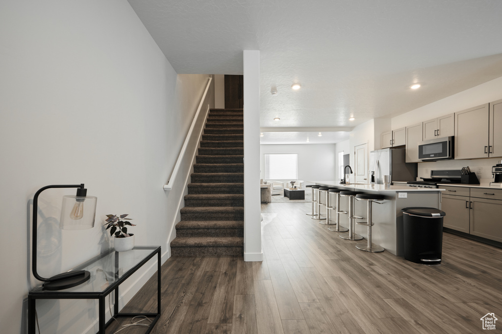 Kitchen with appliances with stainless steel finishes, gray cabinets, a breakfast bar, dark wood-type flooring, and a kitchen island with sink
