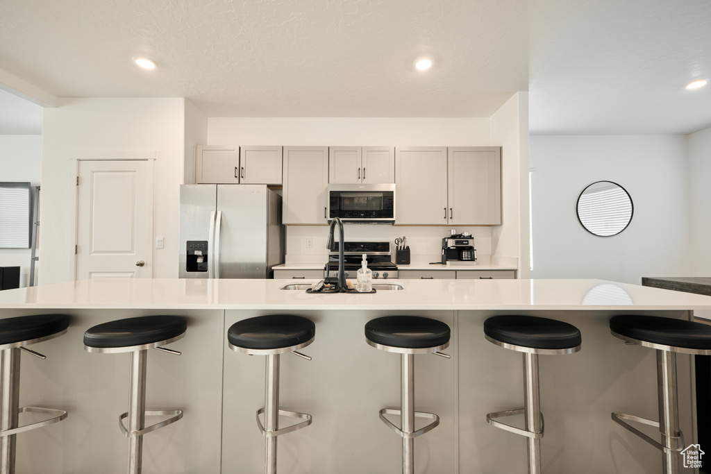 Kitchen with appliances with stainless steel finishes, a sink, light countertops, gray cabinetry, and a kitchen breakfast bar