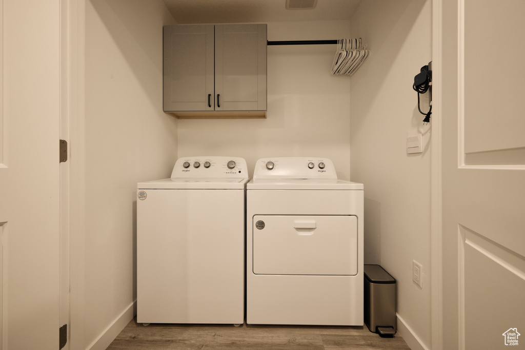 Washroom with independent washer and dryer, cabinet space, wood finished floors, and baseboards