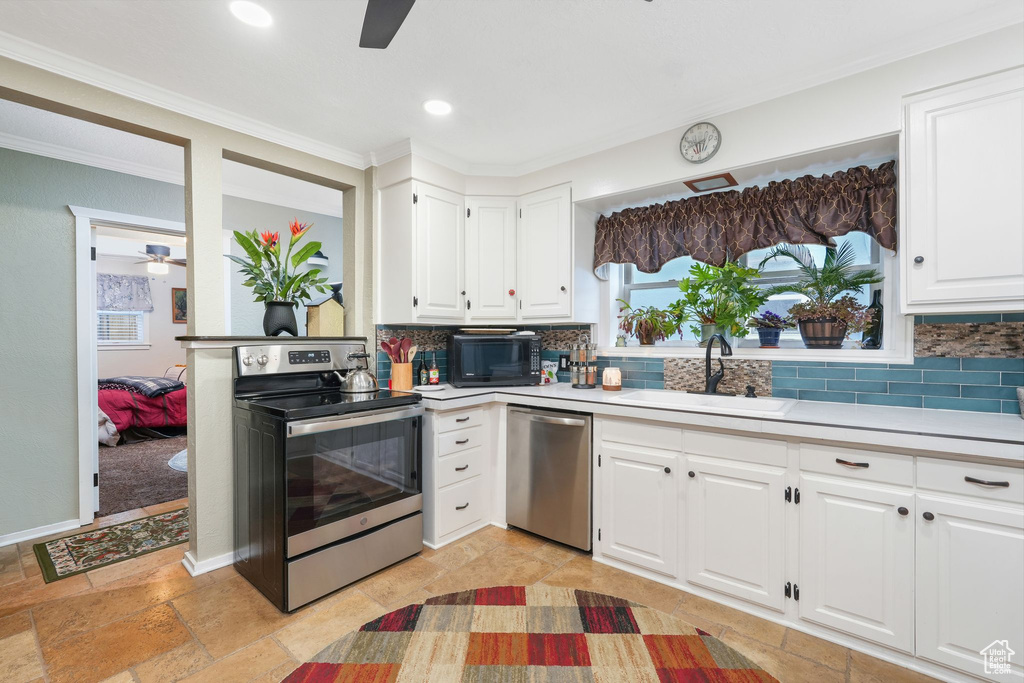 Kitchen with appliances with stainless steel finishes, a ceiling fan, a sink, light countertops, and crown molding