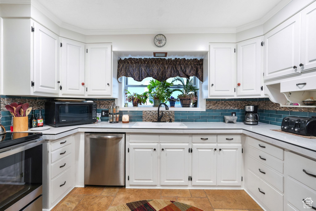 Kitchen with appliances with stainless steel finishes, a sink, light countertops, tasteful backsplash, and ornamental molding