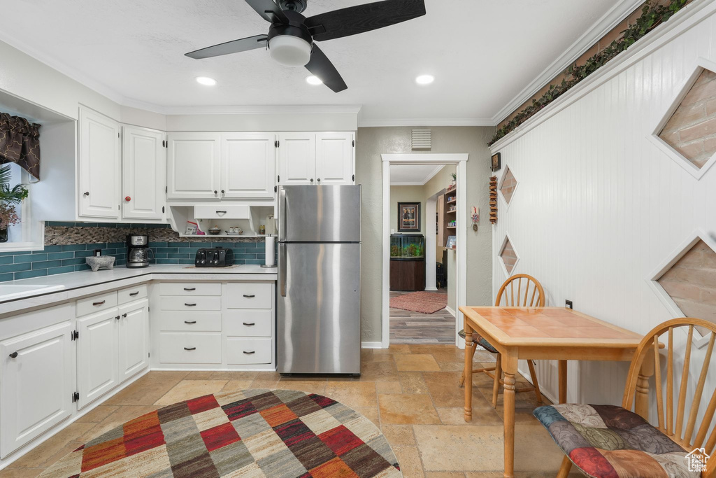 Kitchen featuring freestanding refrigerator, ornamental molding, light countertops, stone tile flooring, and backsplash