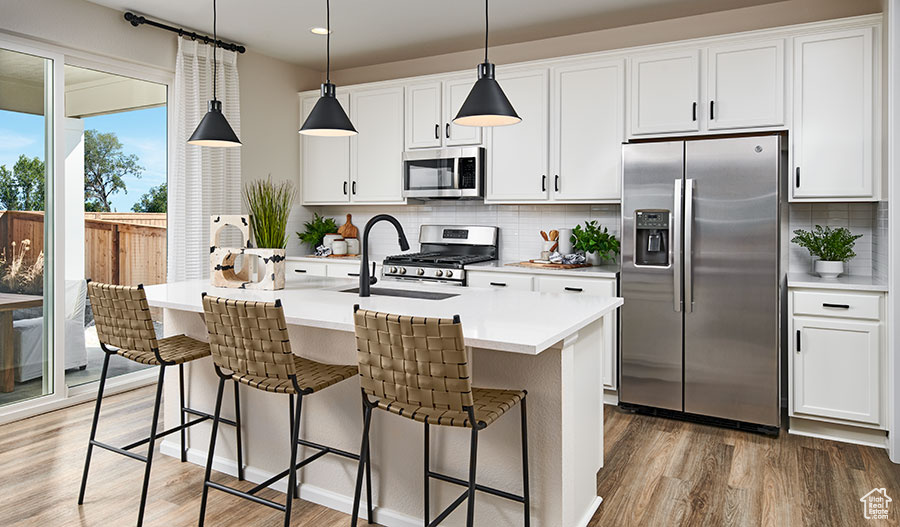 Kitchen with appliances with stainless steel finishes, light wood-style flooring, a sink, decorative backsplash, and a kitchen breakfast bar