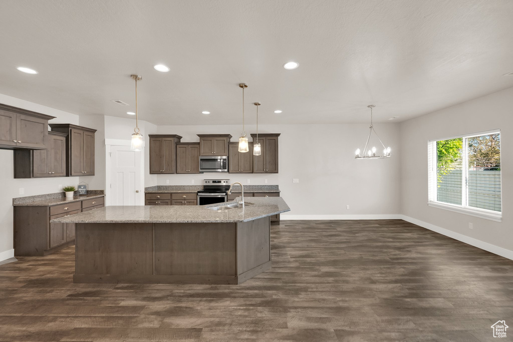 Kitchen featuring stainless steel appliances, recessed lighting, baseboards, a kitchen island with sink, and light stone counters