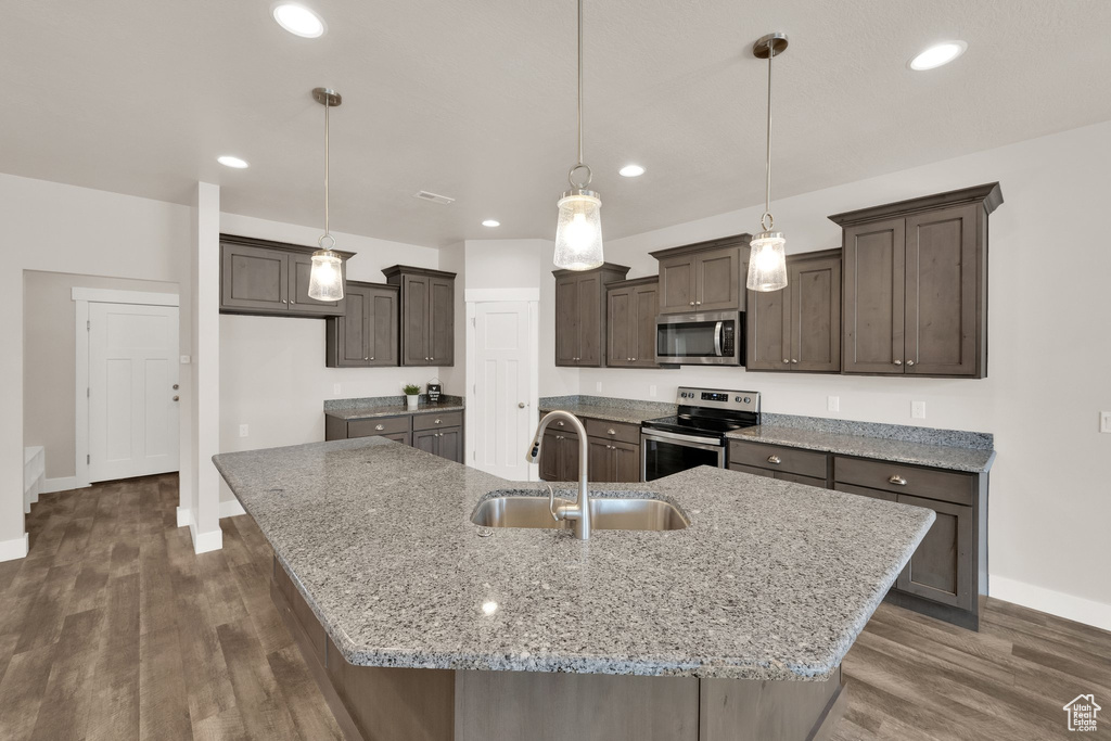 Kitchen with stainless steel appliances, a sink, baseboards, dark brown cabinetry, and a spacious island