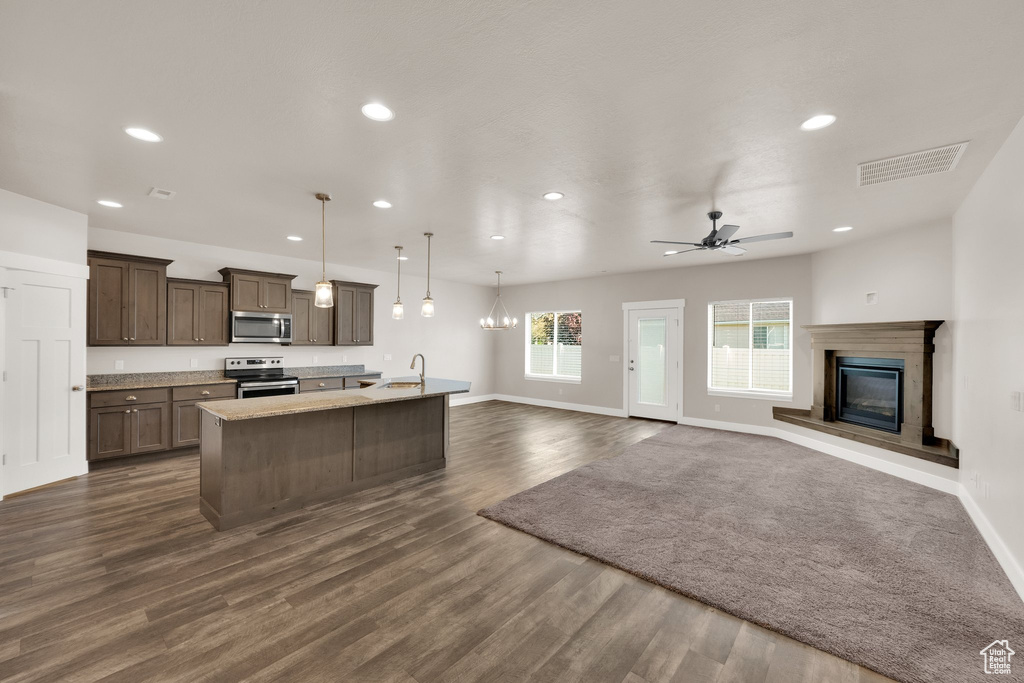 Kitchen with appliances with stainless steel finishes, recessed lighting, baseboards, a kitchen island with sink, and a glass covered fireplace