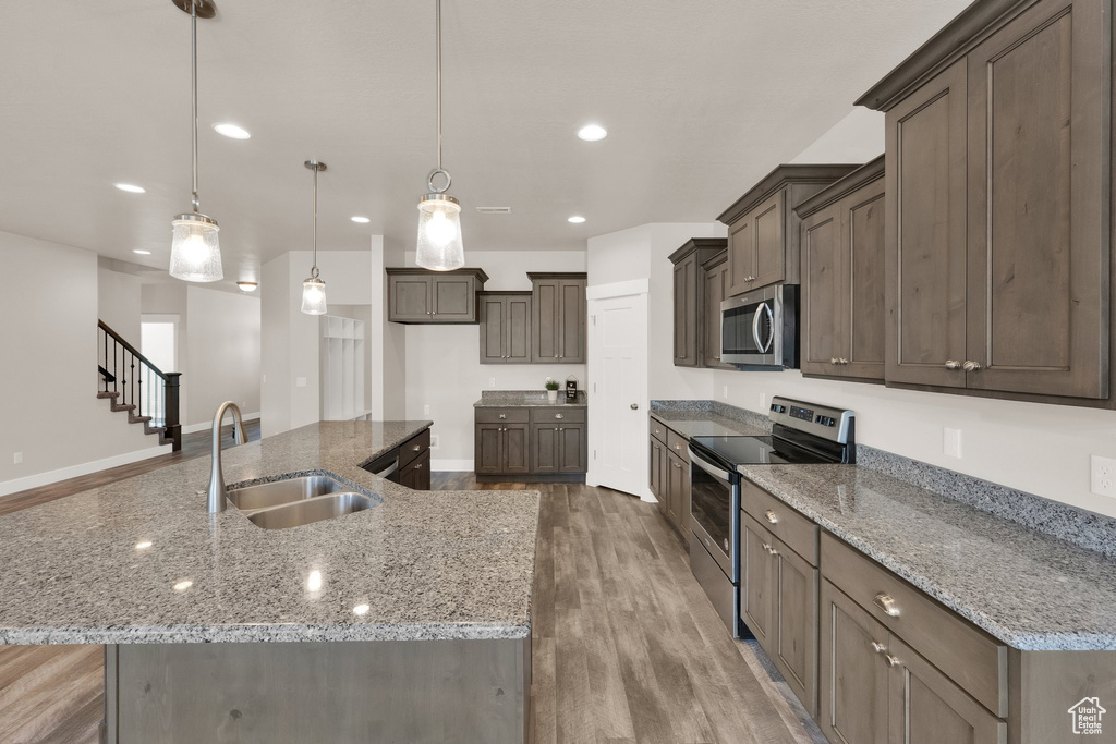 Kitchen with appliances with stainless steel finishes, a sink, light wood finished floors, recessed lighting, and a spacious island