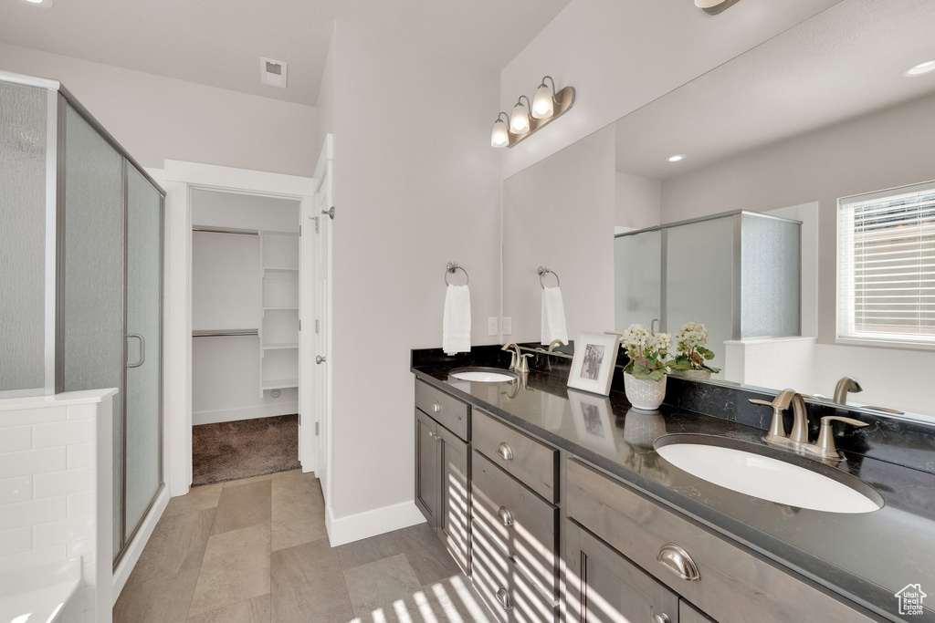 Bathroom featuring a shower stall, double vanity, a walk in closet, and baseboards