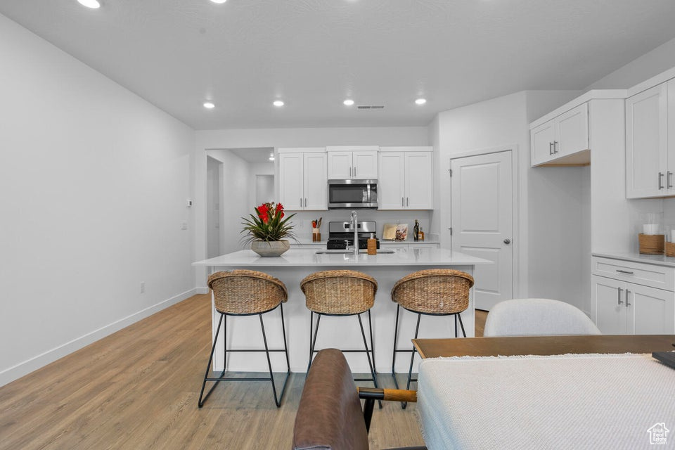 Kitchen with stainless steel appliances, light wood-type flooring, baseboards, a kitchen bar, and white cabinetry