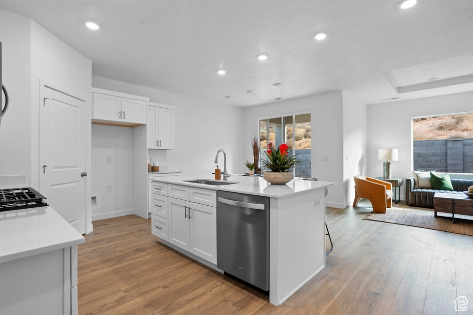 Kitchen with stainless steel dishwasher, a sink, light wood finished floors, white cabinetry, and recessed lighting