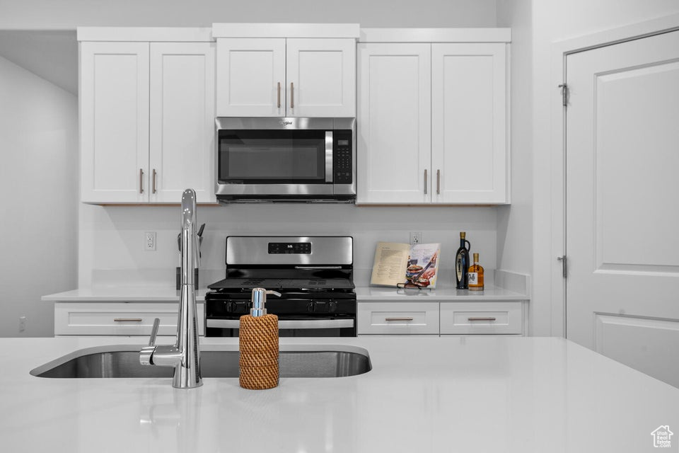 Kitchen with appliances with stainless steel finishes, light countertops, white cabinetry, and a sink