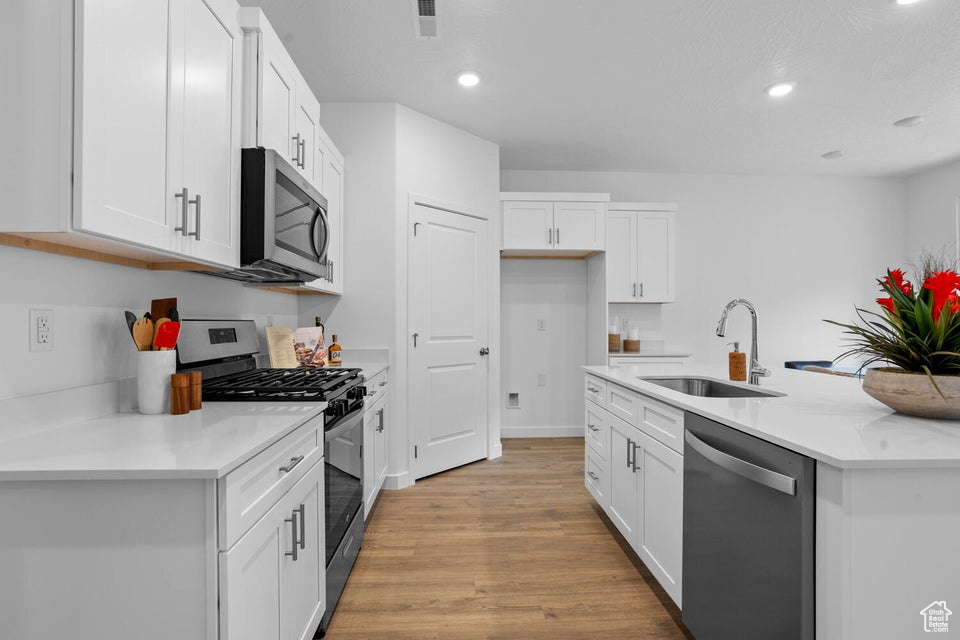 Kitchen featuring stainless steel appliances, a sink, recessed lighting, light wood-style flooring, and white cabinetry