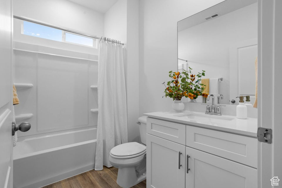 Bathroom featuring wood finished floors, toilet, vanity, and shower / bath combo with shower curtain