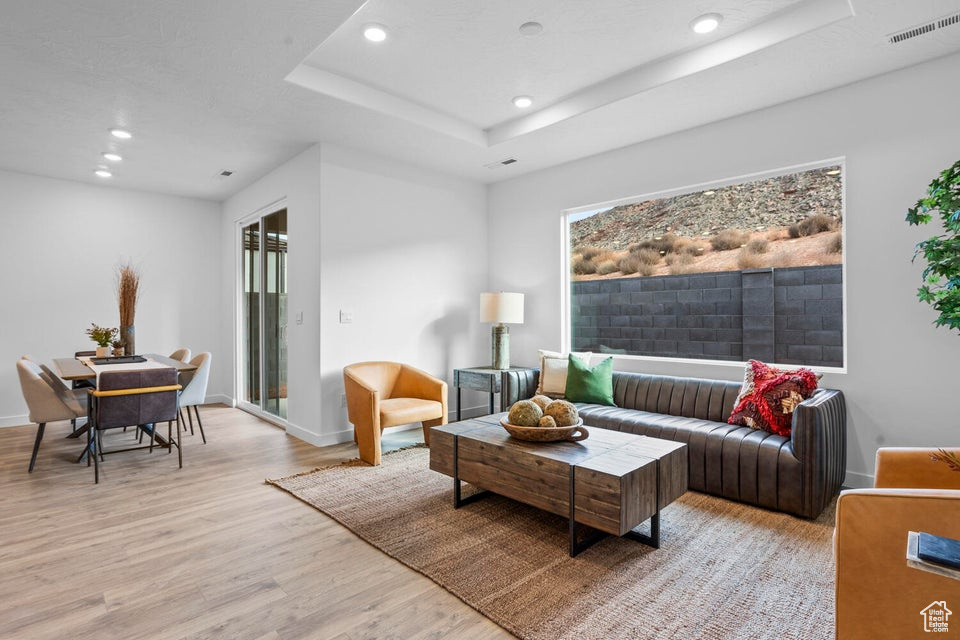 Living room featuring recessed lighting, light wood-type flooring, a tray ceiling, and baseboards