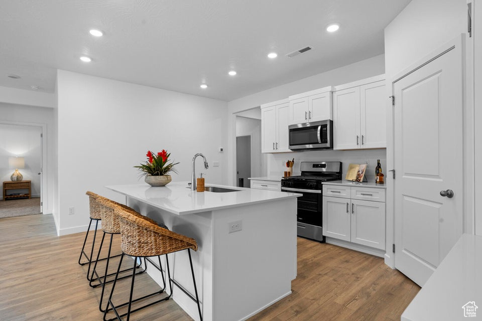 Kitchen featuring stainless steel appliances, a sink, an island with sink, a kitchen breakfast bar, and recessed lighting