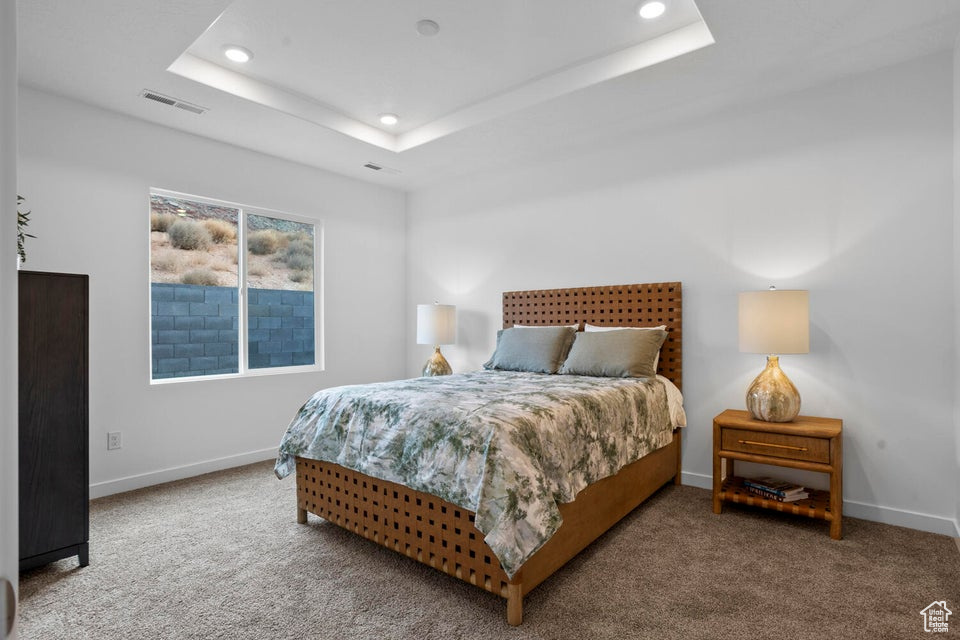 Carpeted bedroom with a raised ceiling, recessed lighting, and baseboards