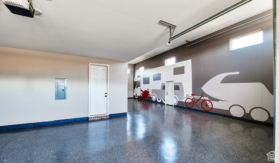 Garage with a garage door opener, electric panel, and baseboards