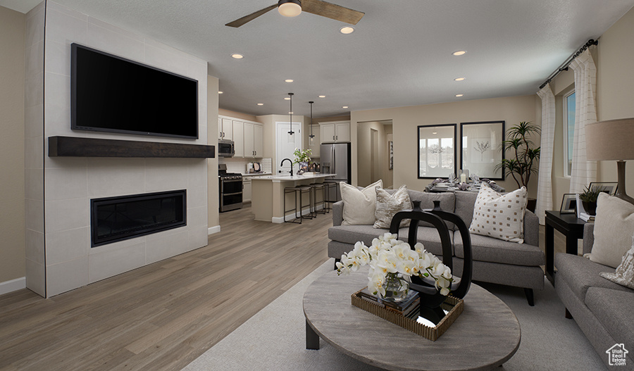 Living room with light wood-style floors, ceiling fan, recessed lighting, baseboards, and a tile fireplace