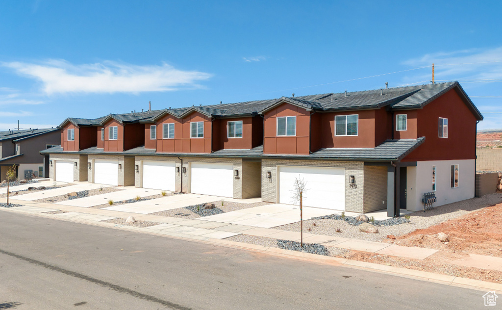 Townhome / multi-family property with a garage, driveway, a residential view, and stucco siding