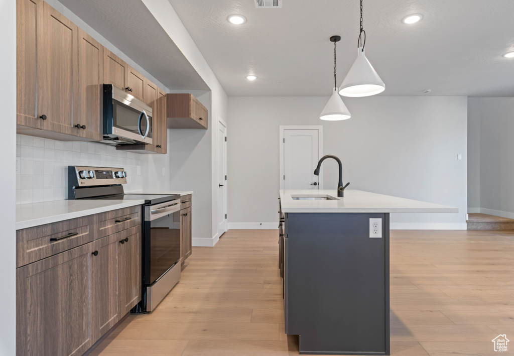 Kitchen with appliances with stainless steel finishes, a sink, baseboards, light wood-style flooring, and recessed lighting