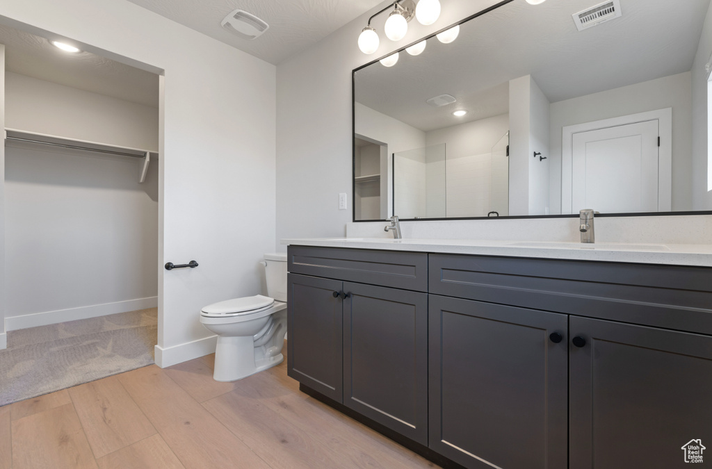Bathroom with wood finished floors, toilet, baseboards, double vanity, and a spacious closet