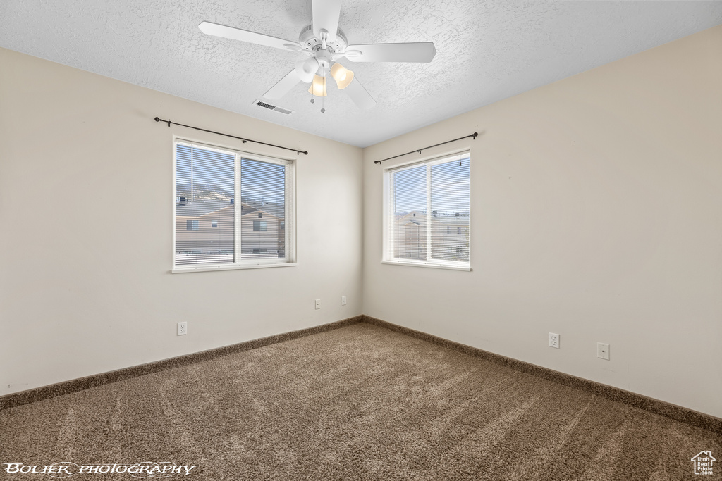 Carpeted spare room featuring a textured ceiling, ceiling fan, and baseboards