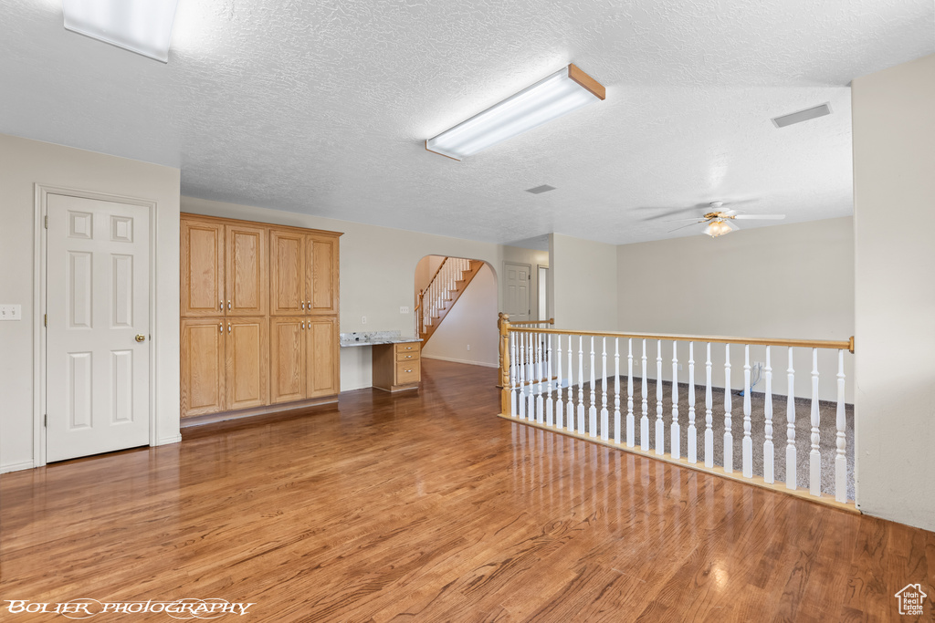 Empty room with light wood-style floors, ceiling fan, arched walkways, and a textured ceiling
