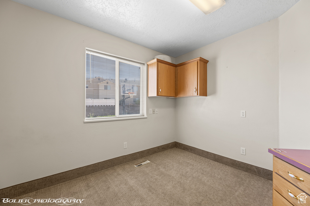 Carpeted empty room with a textured ceiling and baseboards