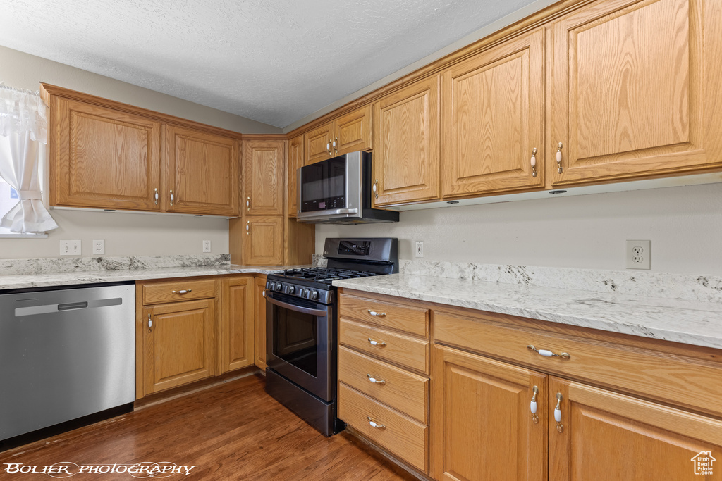 Kitchen featuring stainless steel appliances, wood finished floors, light stone counters, and a textured ceiling