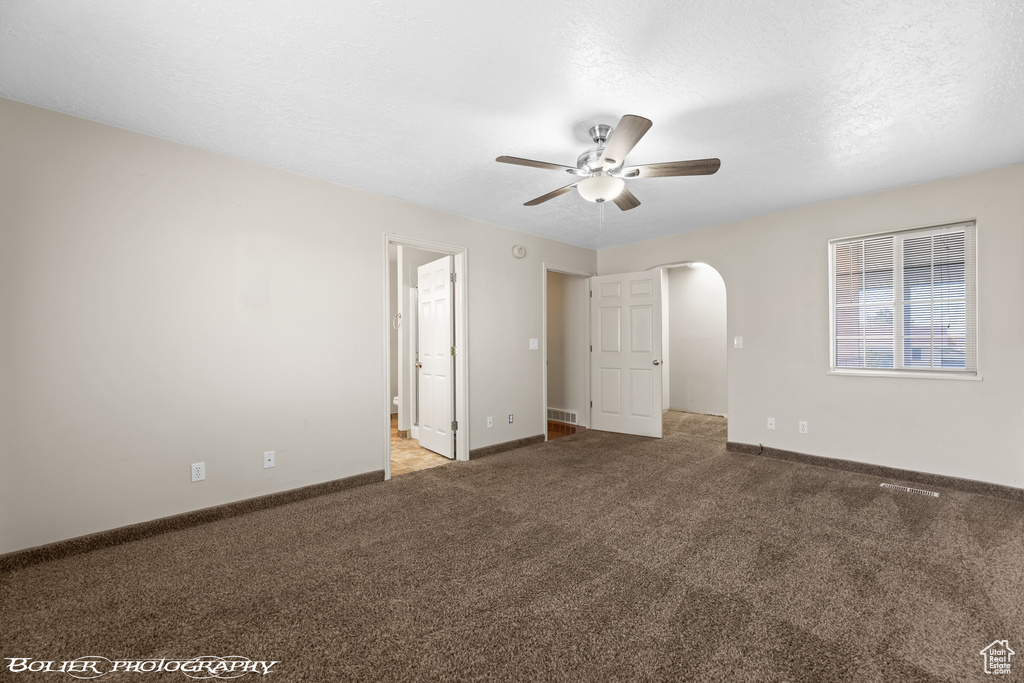 Unfurnished bedroom with arched walkways, carpet floors, baseboards, connected bathroom, and a ceiling fan